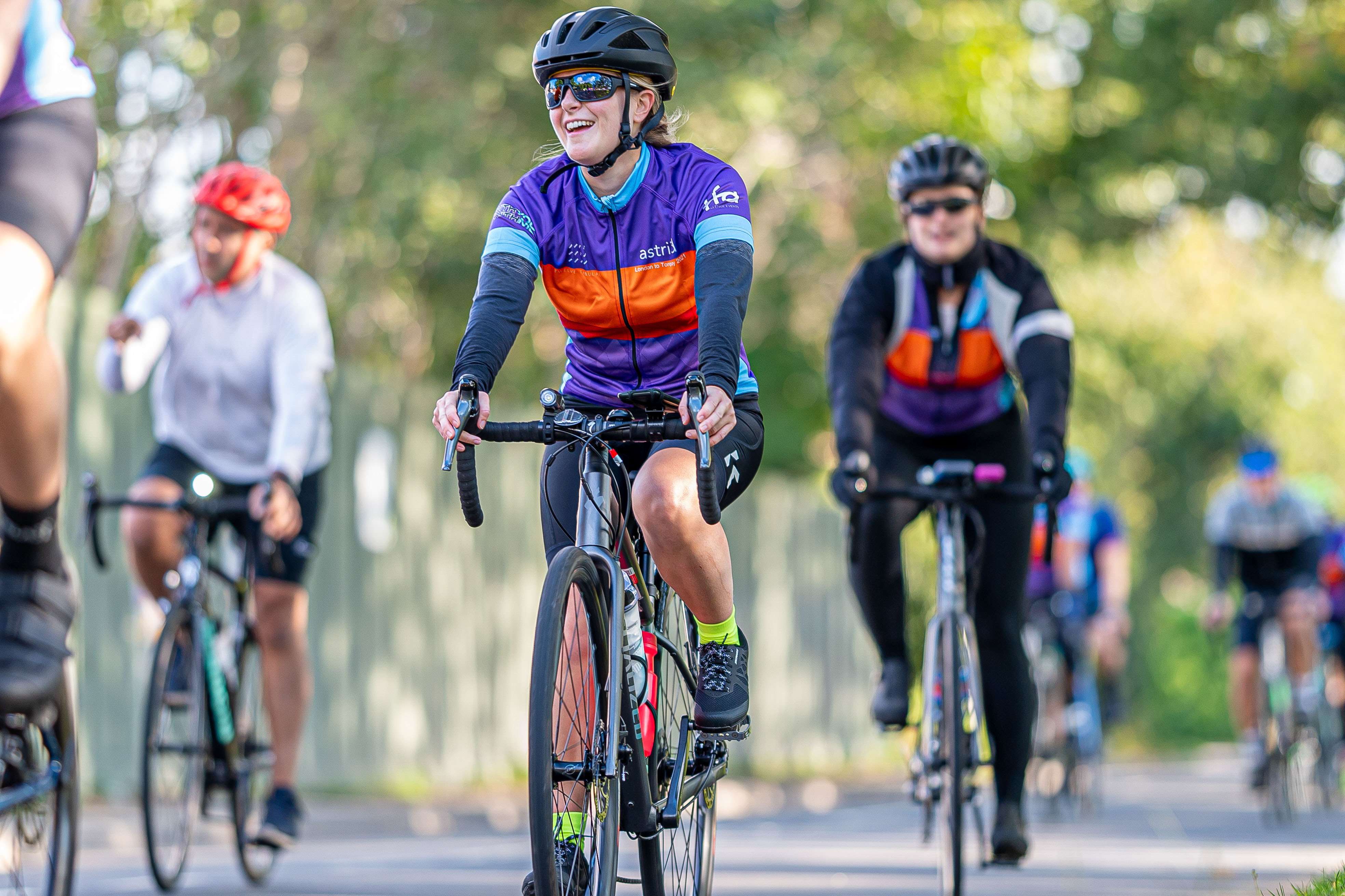 Cyclist smiling with groups of blurred out team mates on a tree lines sunny street