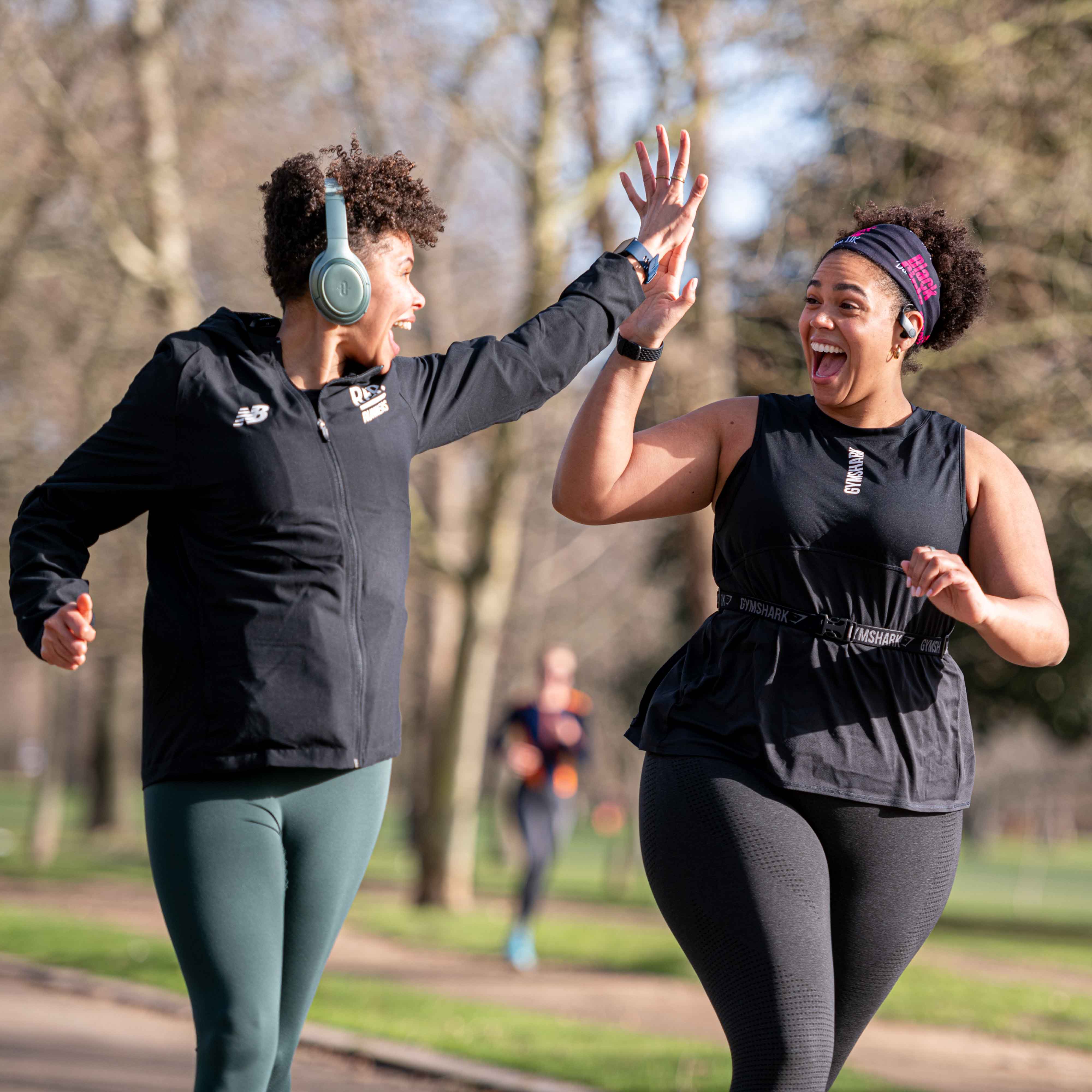 Two women running in a park on a sunny morning high five and smile at each other.