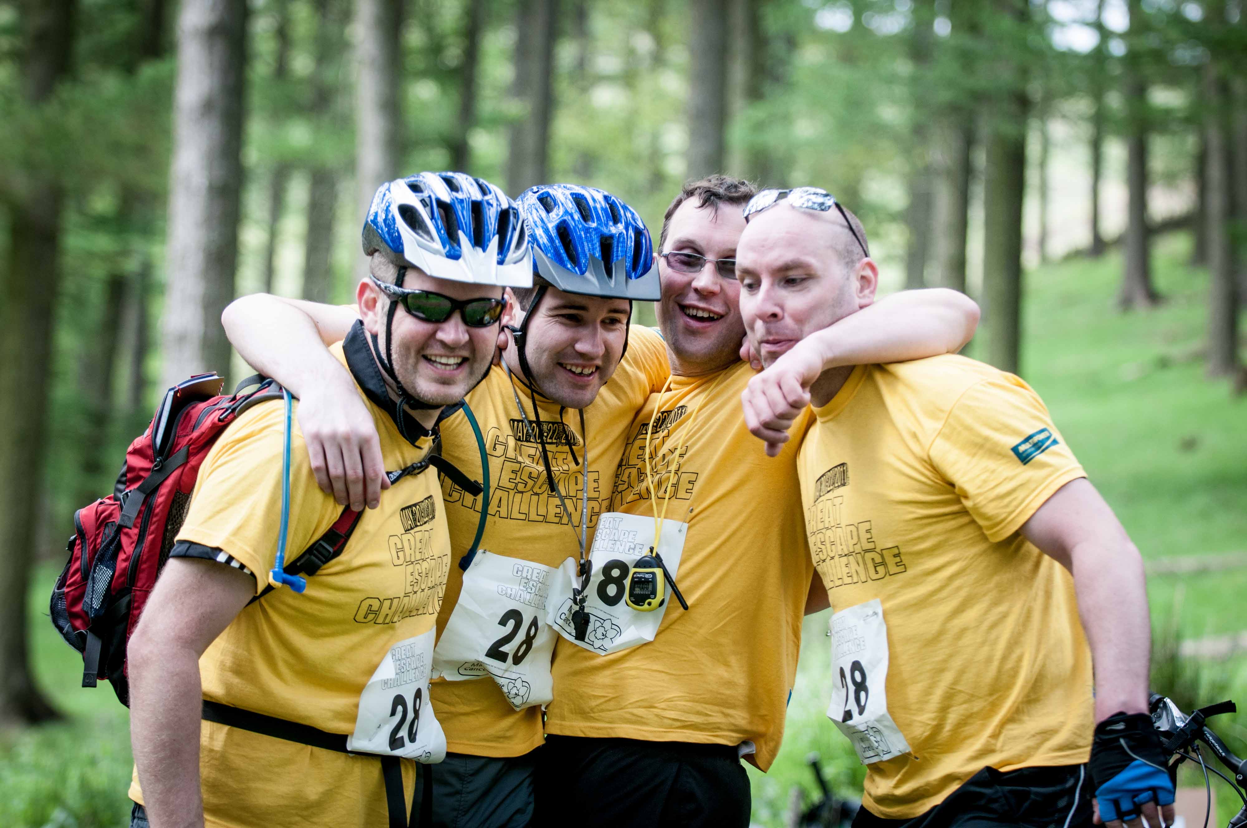 A team of four men outdoors in a wooded area smile and pose for a group photo