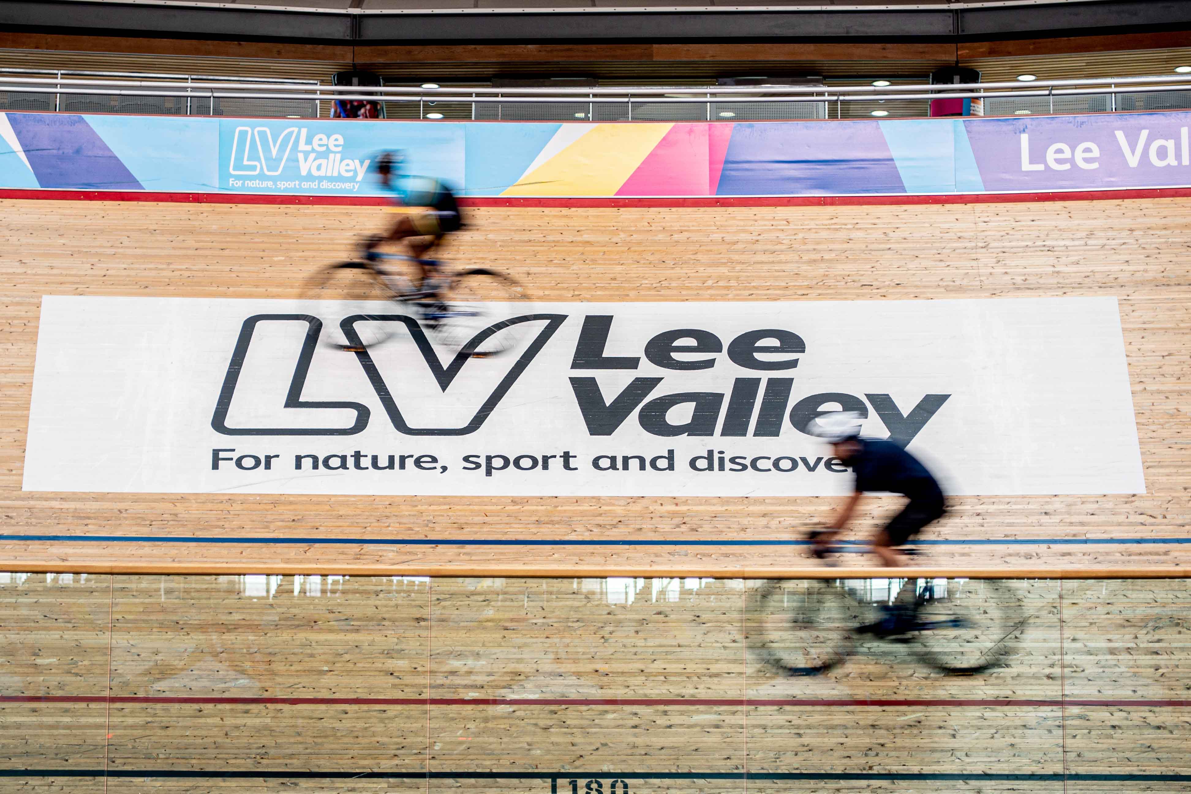Two cyclists ride race at an indoor Velodrome.